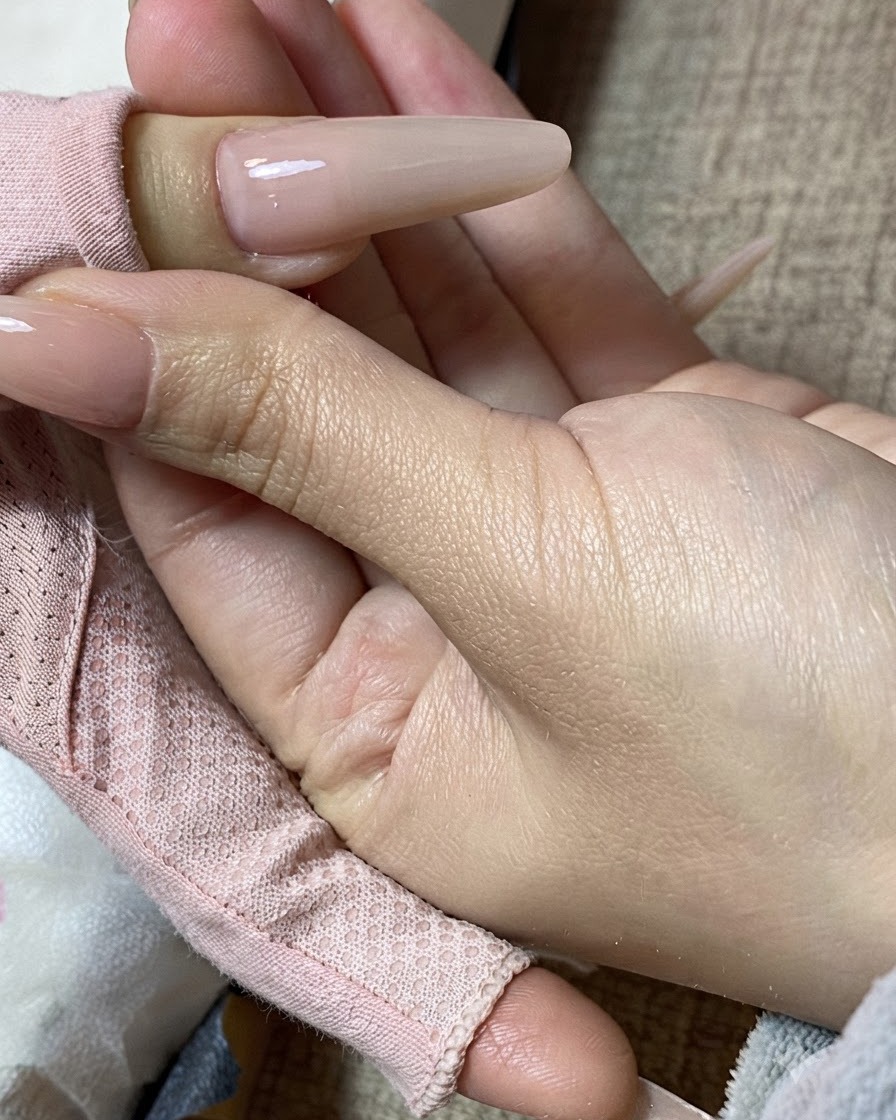 A close-up view of a hand holding a finished milk tea manicured nail.