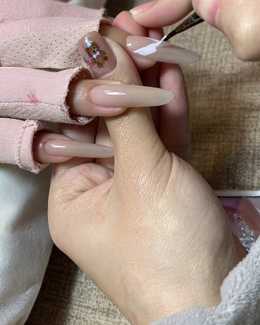 A nail artists hand refining white butterfly wing patterns on an elongated nail.