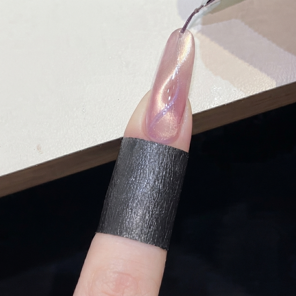 A cylindrical magnet held near a purple cat-eye line on a pink shimmering nail.