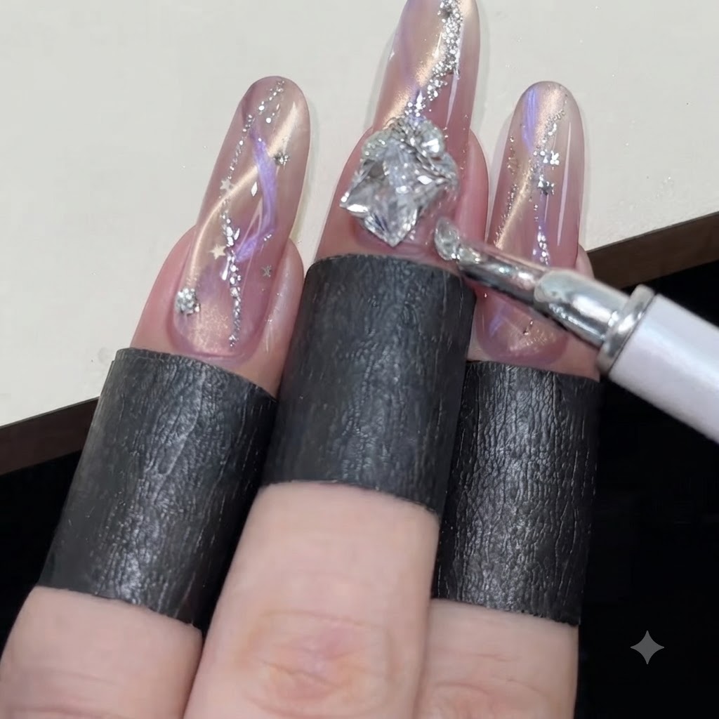 A wax pen arranging small round rhinestones around a larger diamond-shaped gem on a sparkling pink cat-eye nail.