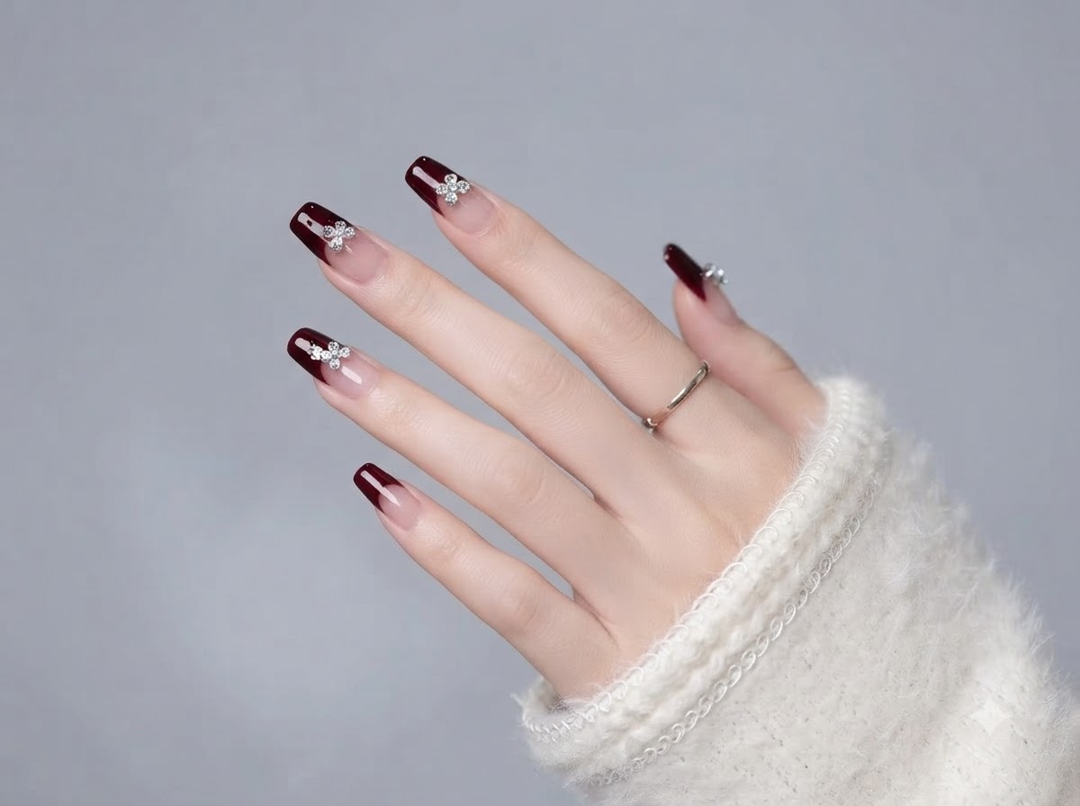A hand showing the complete layout of burgundy and nude gel nails with crystal details.