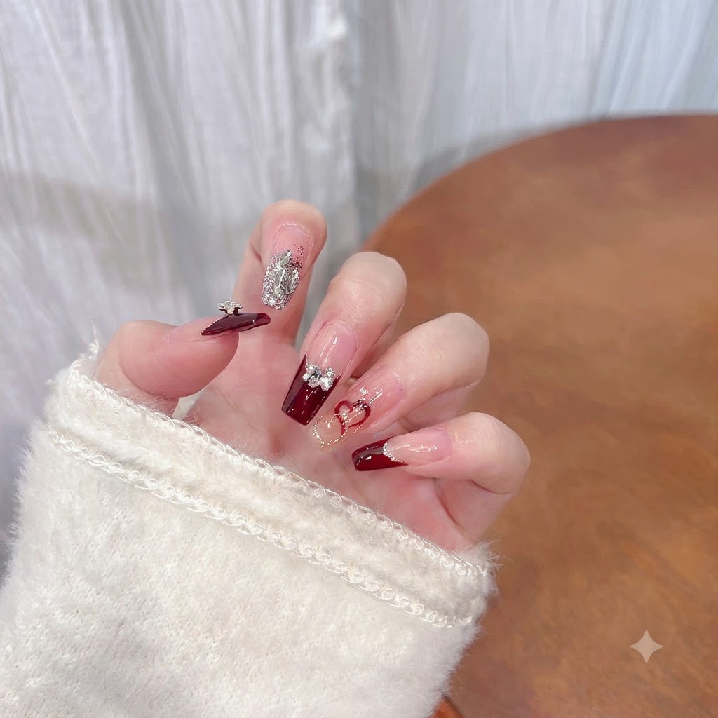 A close-up of the middle finger showcasing a dark burgundy base with rhinestones and a silver bow.