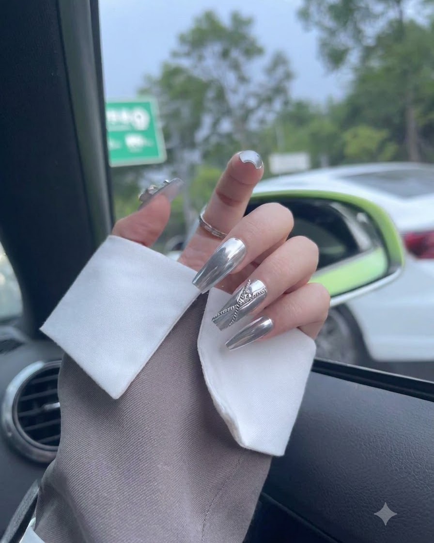 A close-up view of fingers showing textured silver chrome nail finishes and embedded elements.