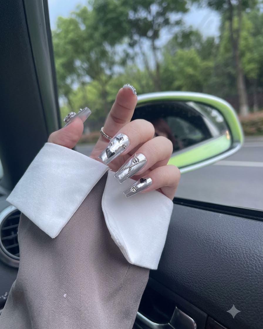 Fingers softly moving in daylight to display silver metallic press-on nails adorned with a dangling chain.