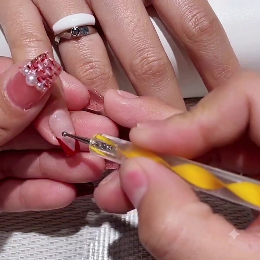 A yellow-handled dotting tool placing two small red dots into the clear negative space of a V-tip nail.