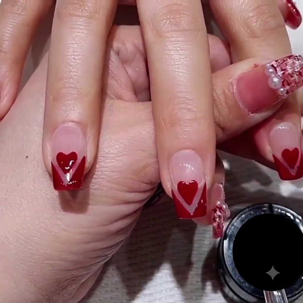 A close-up of a nail artists hand using a thin striper brush to draw a fine rose-gold glitter line along the edge of a red V-tip nail design.