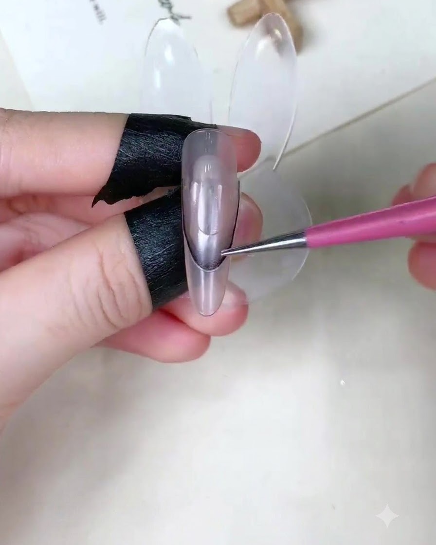 A close-up of a finger holding a curved guide sticker on a clear nail display stand.