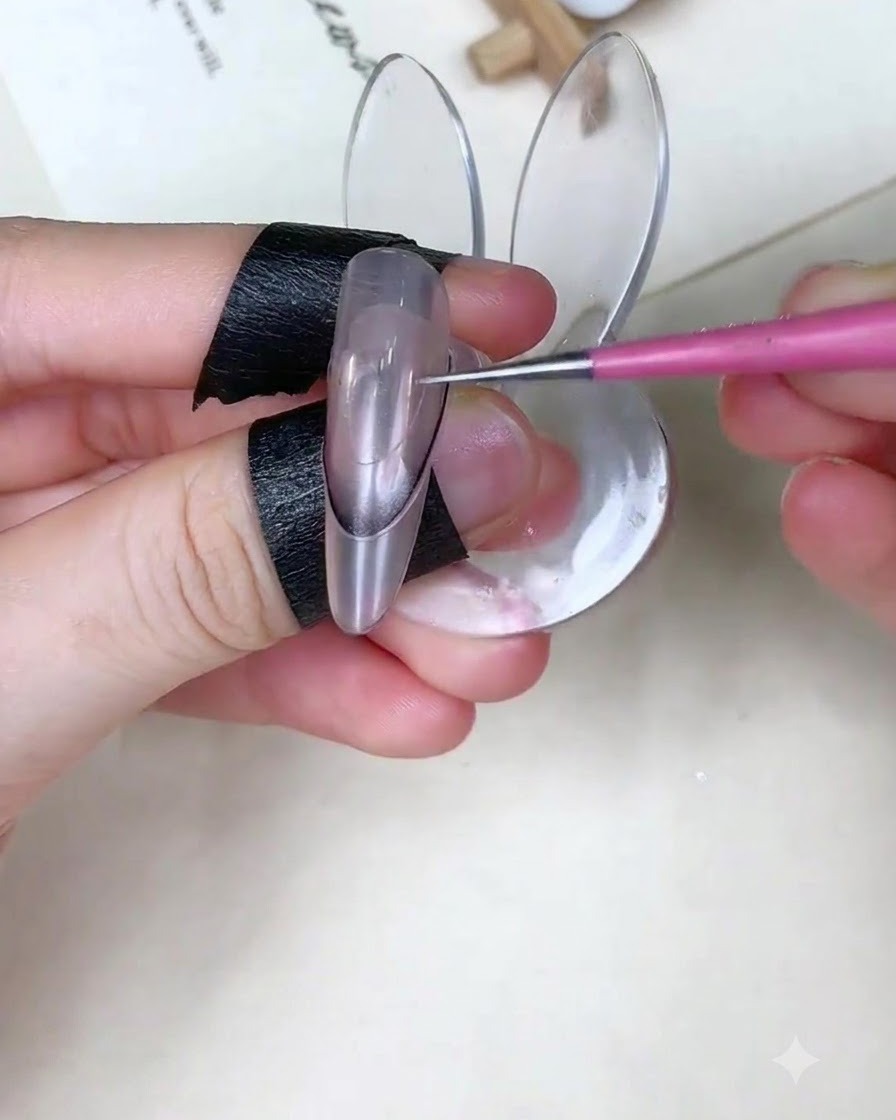 A nail brush applying baby blue gel onto the upper portion of a nail over a guide sticker.