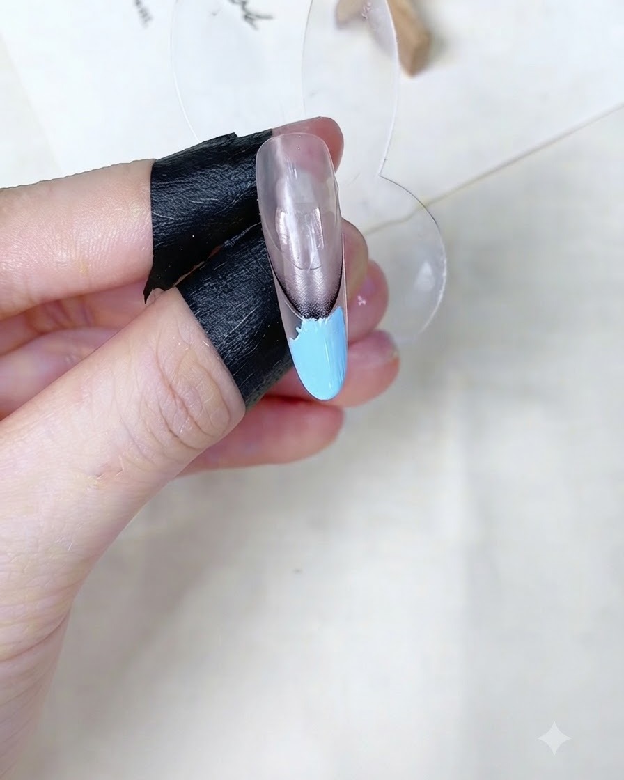 A makeup sponge dabbing the baby blue gel area on a nail display stand.