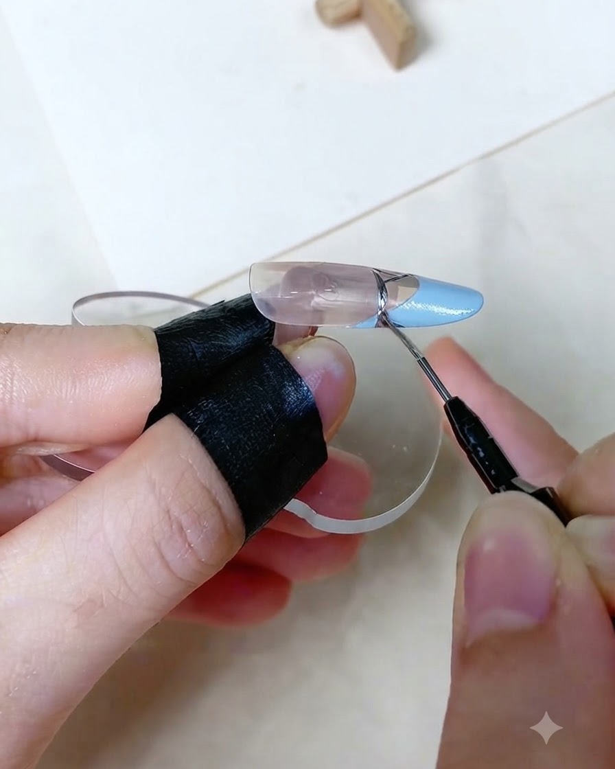 A close-up view of a fine detailing brush drawing a precise silver metallic line across the transition of a baby blue French tip on an artificial nail display finger.