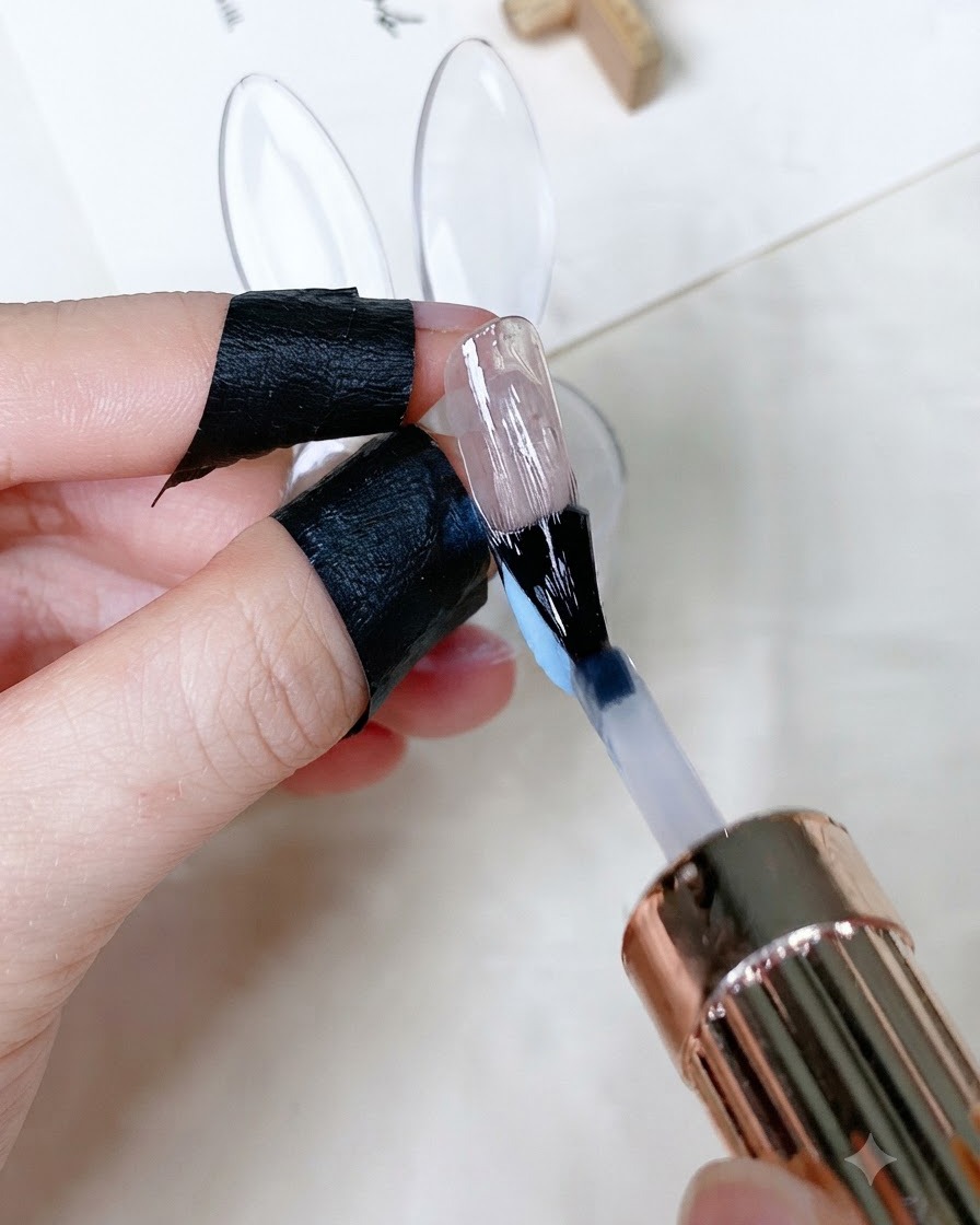 A brush applying a clear glossy top coat over a painted fingernail.