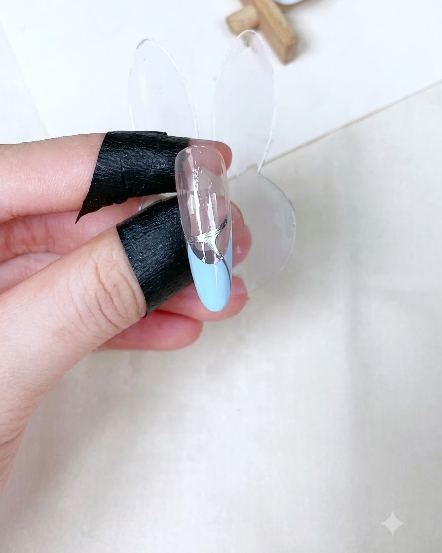 A single sculpted nail stand showing a cured glossy clear top coat with silver detailing over a baby blue French tip.