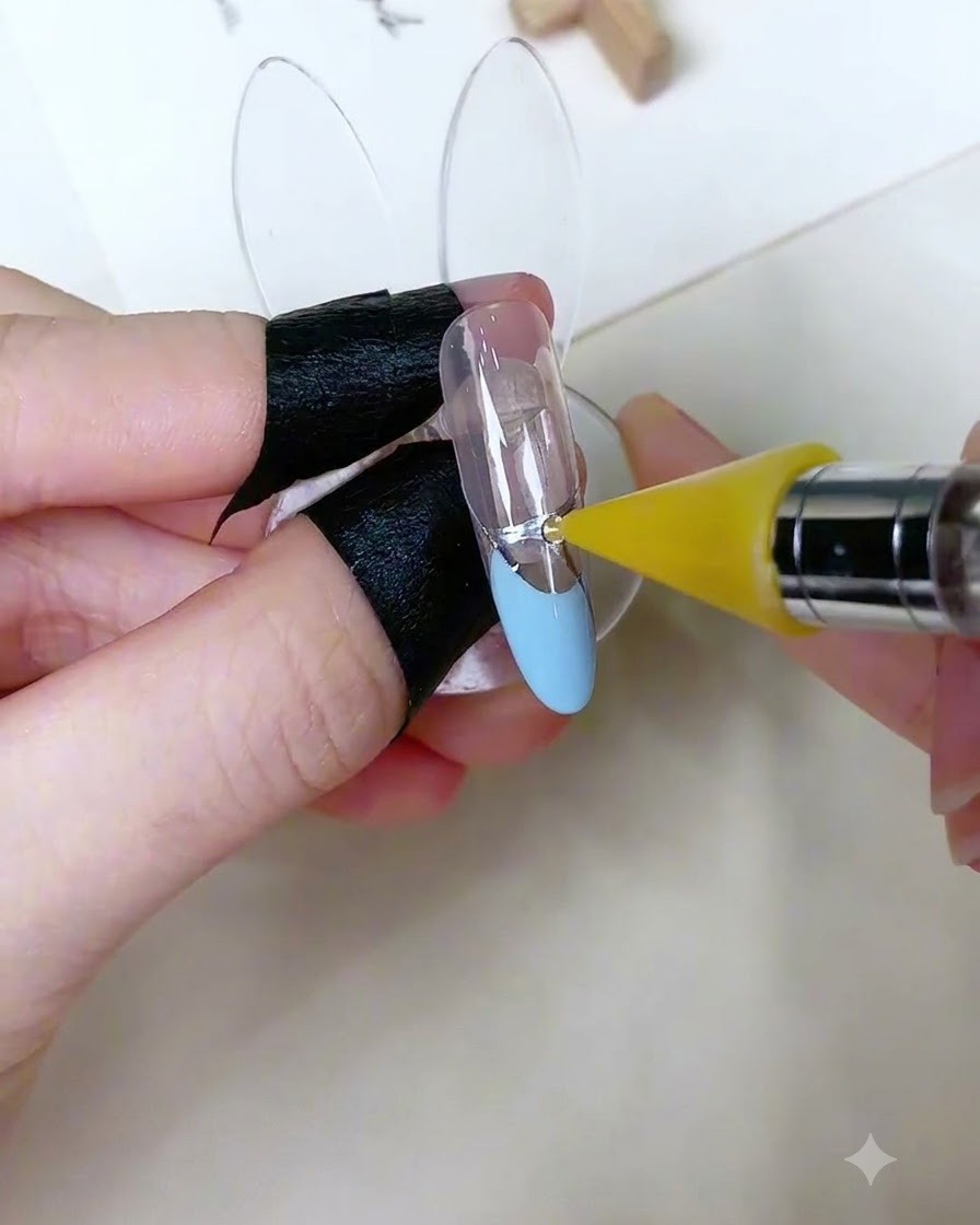 A specialized pickup tool placing a small round rhinestone onto a dot of adhesive gel on a decorated nail.