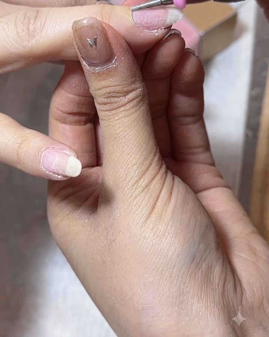 An e-file clearing the lateral nail folds on a thumb during cuticle prep.