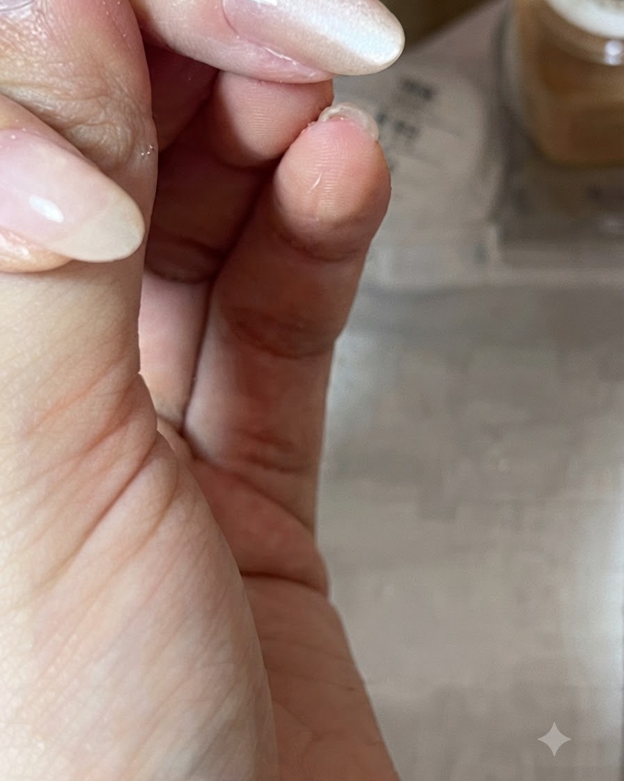 A close-up of a hand holding a magnetic wand diagonally over a glossy nude gel-polished nail to shape the cat-eye light reflection.