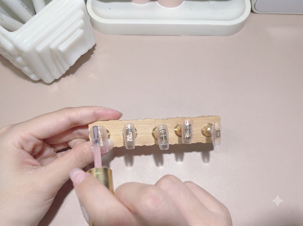 A brush applying a translucent milk tea colored gel polish onto a nail tip.