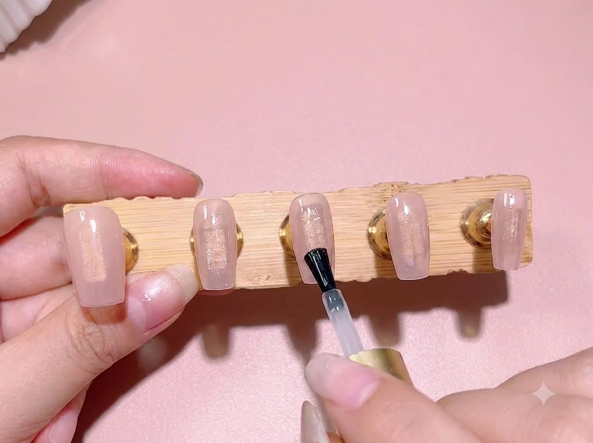 A standard polish brush applying a layer of clear blooming gel over a translucent pink base color on a nail tip.