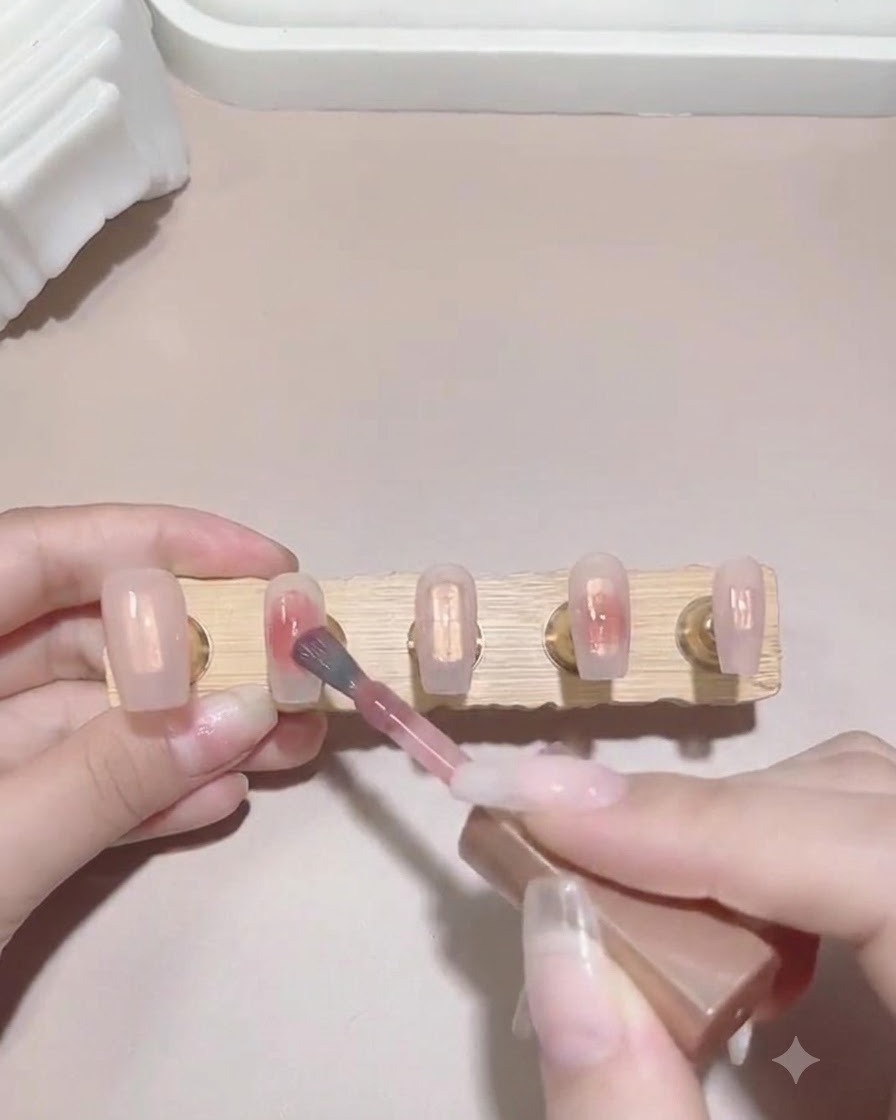 A brush dabbing a small drop of pink gel polish onto the wet surface of a nail tip to begin creating a gradient effect.