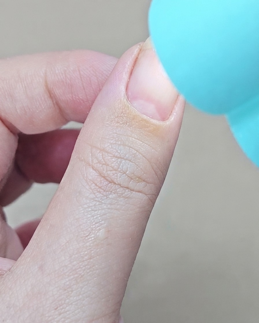 A handheld blue UV lamp positioned directly over a finger to cure the gel base coat.