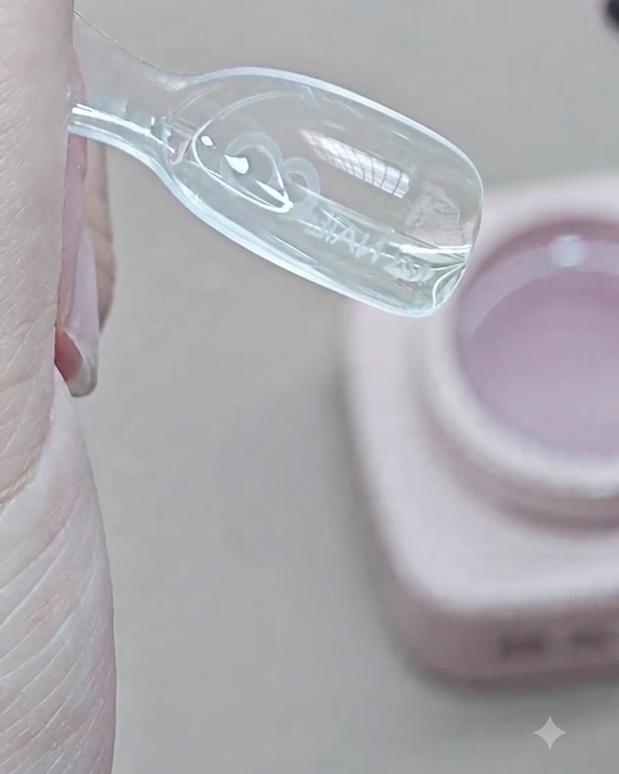 A brush placing transparent extension gel into the inner well of a clear dual form mold.