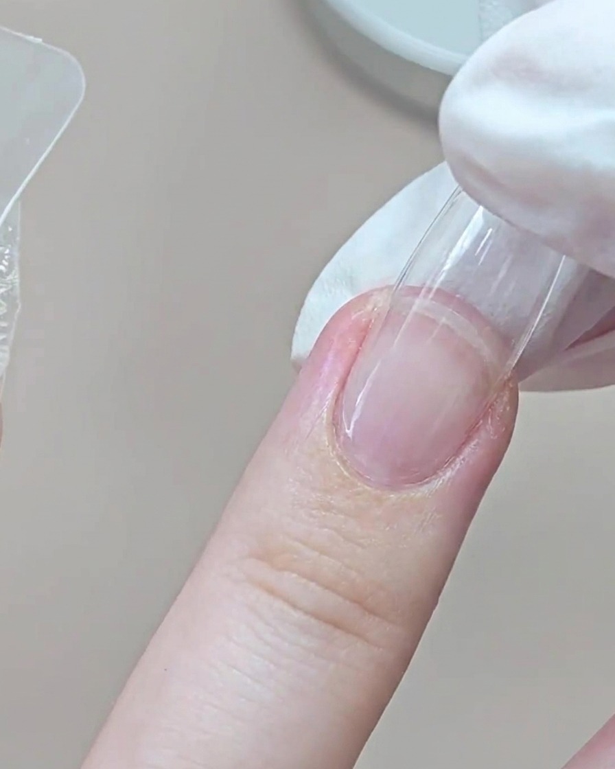 A gloved finger pressing a transparent dual form onto the ring finger near the cuticle area.