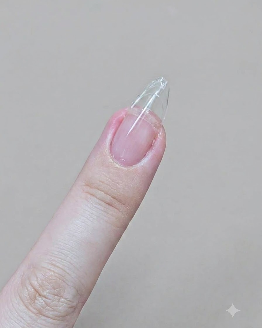 A finger with a clear gel extension being filed into a sharp almond shape with an emery board.
