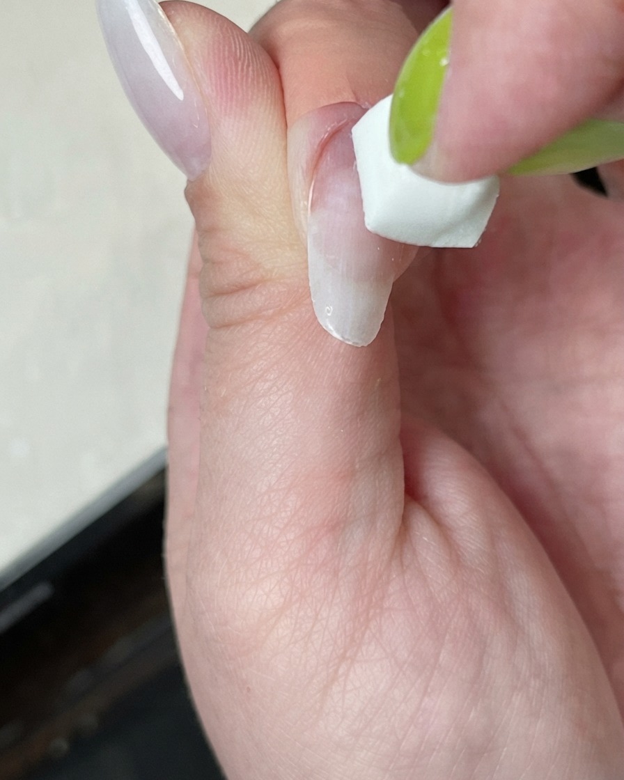 A nail being cured under a mini curing lamp with a white light glow.
