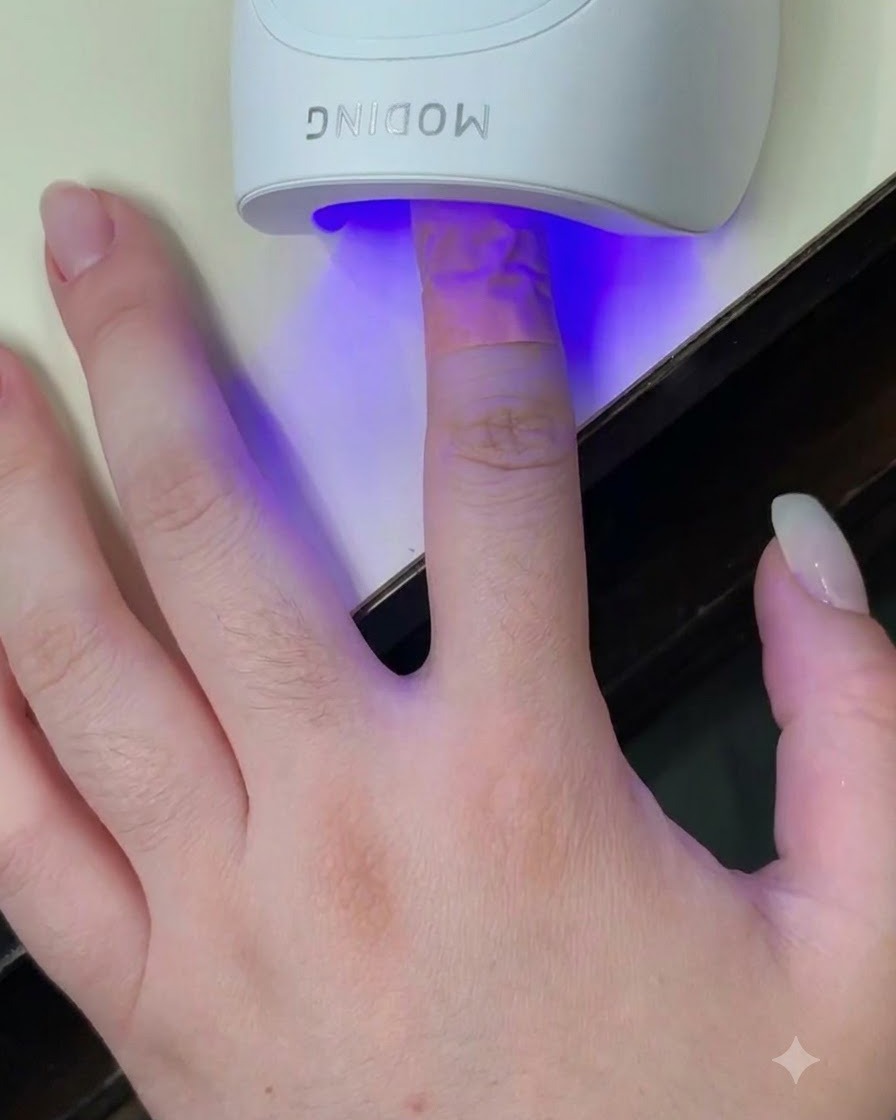 A finger placed inside a white mini UV LED curing lamp with a blue light shining on the nail.