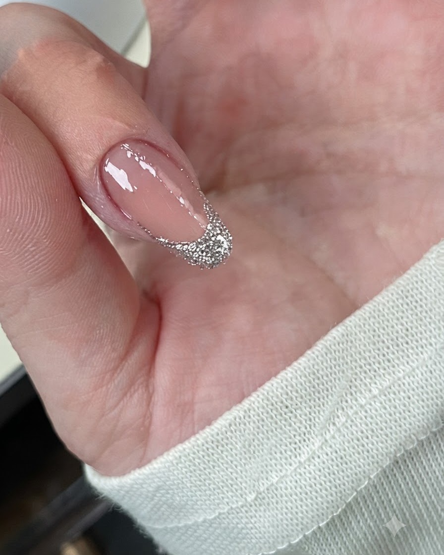 A close-up of a fingernail showing chunky silver glitter layered densely over the French tip.