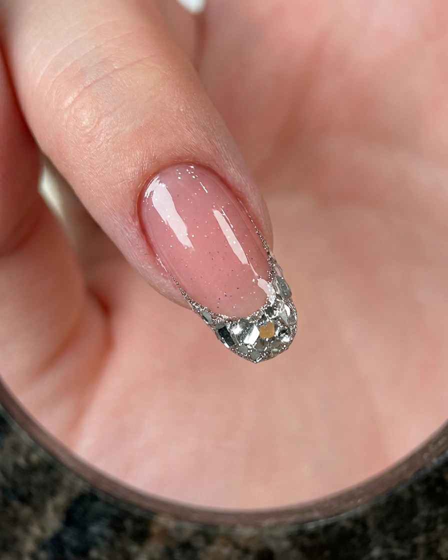 A close-up view of a finger showing a French tip filled with chunky silver glitter over a pink base.