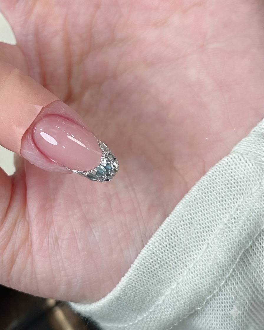 A pair of tweezers gently pinching the sidewalls of a gel-coated nail while under a lamp.