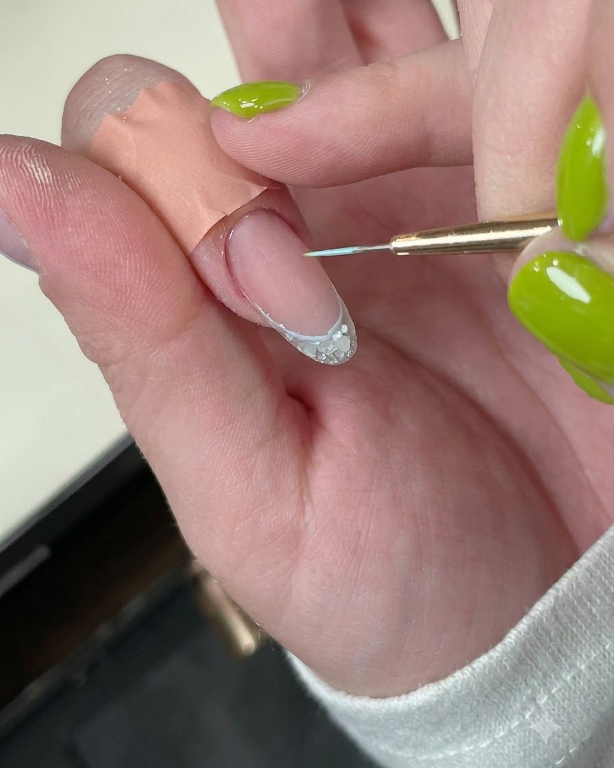 A fingernail with a delicate blue border line placed under a mini LED curing lamp.