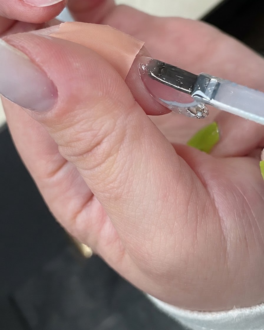 A hand curing the finished manicure inside a compact white UV nail lamp.