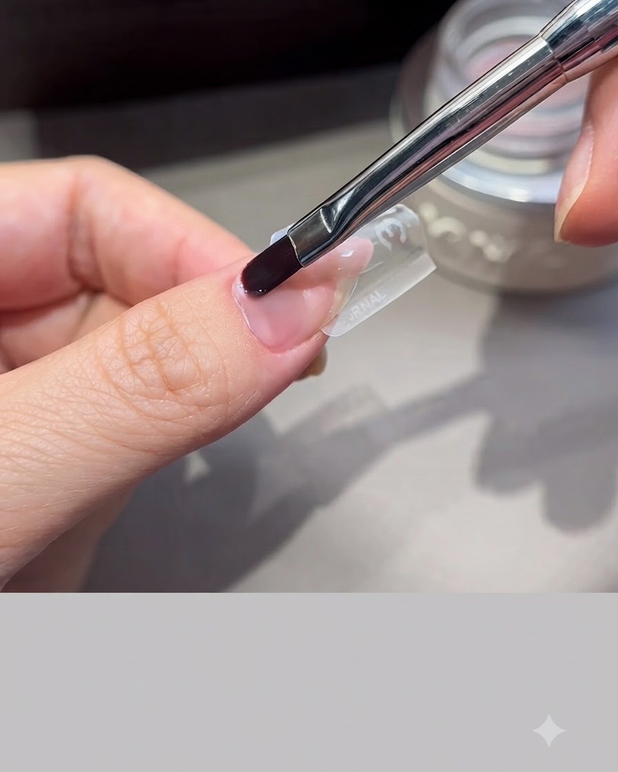 A professional nail brush smoothing extension gel over a clear nail mold form positioned on a finger.
