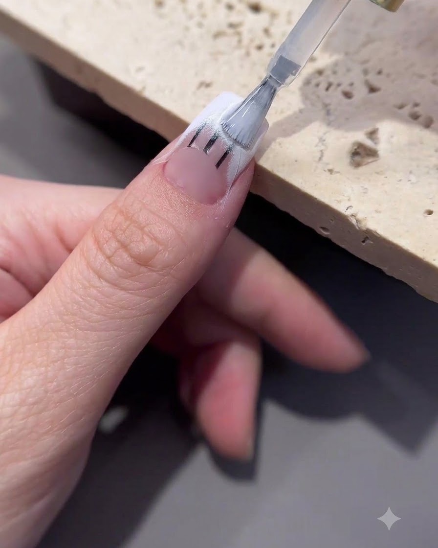 A brush applying transfer gel onto the tip area of a decorated nail.