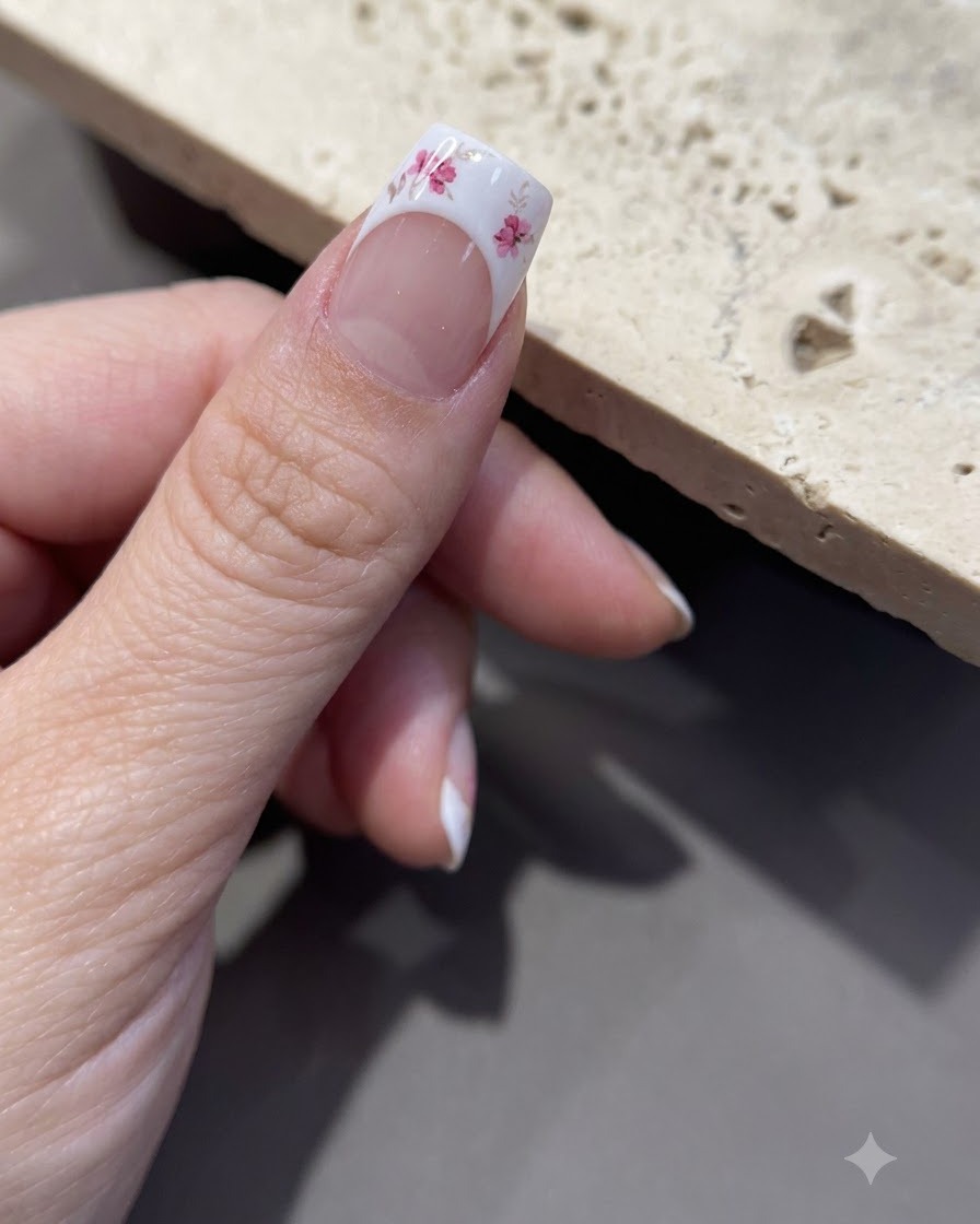 A close-up of tweezers peeling backing paper off a floral sticker sheet.