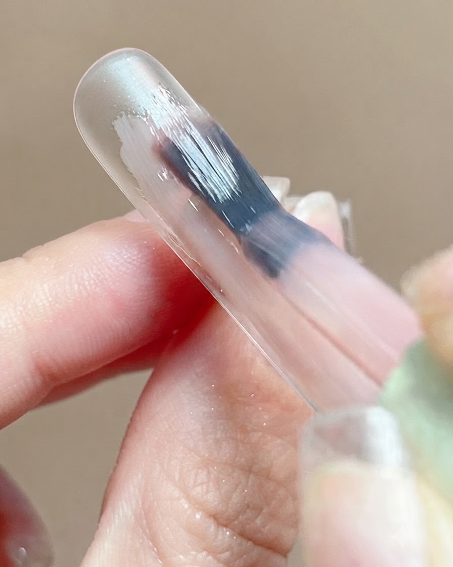 A close-up of a pink gel base coat reflecting light smoothly on a nail surface during self-leveling.