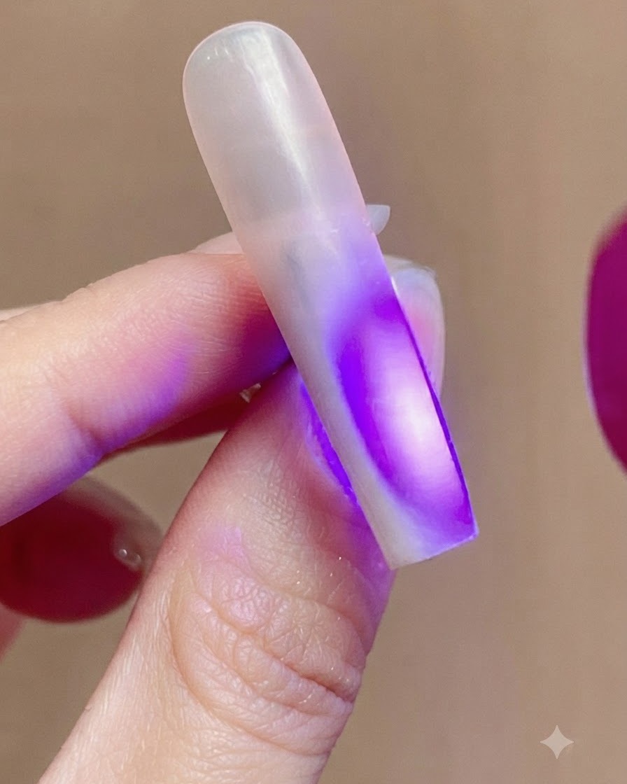 A fingernail illuminated by purple UV light from a nail lamp during the curing process.