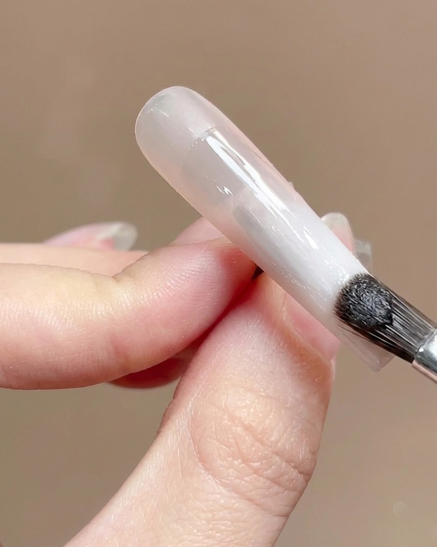 A nail brush applying a clear, glossy top coat over a gradient nail surface.