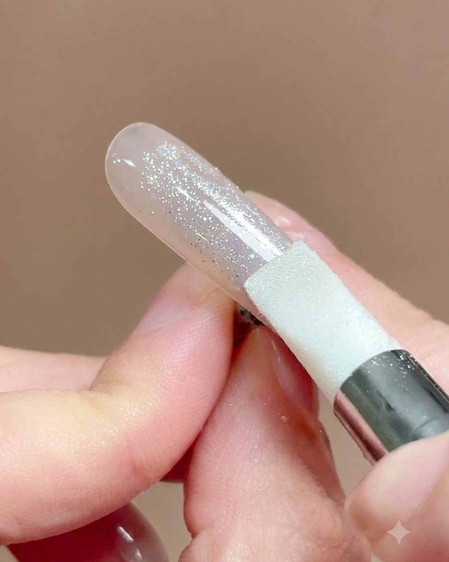 A silicone pen tool being pressed and rubbed across a nail surface covered in chrome powder.