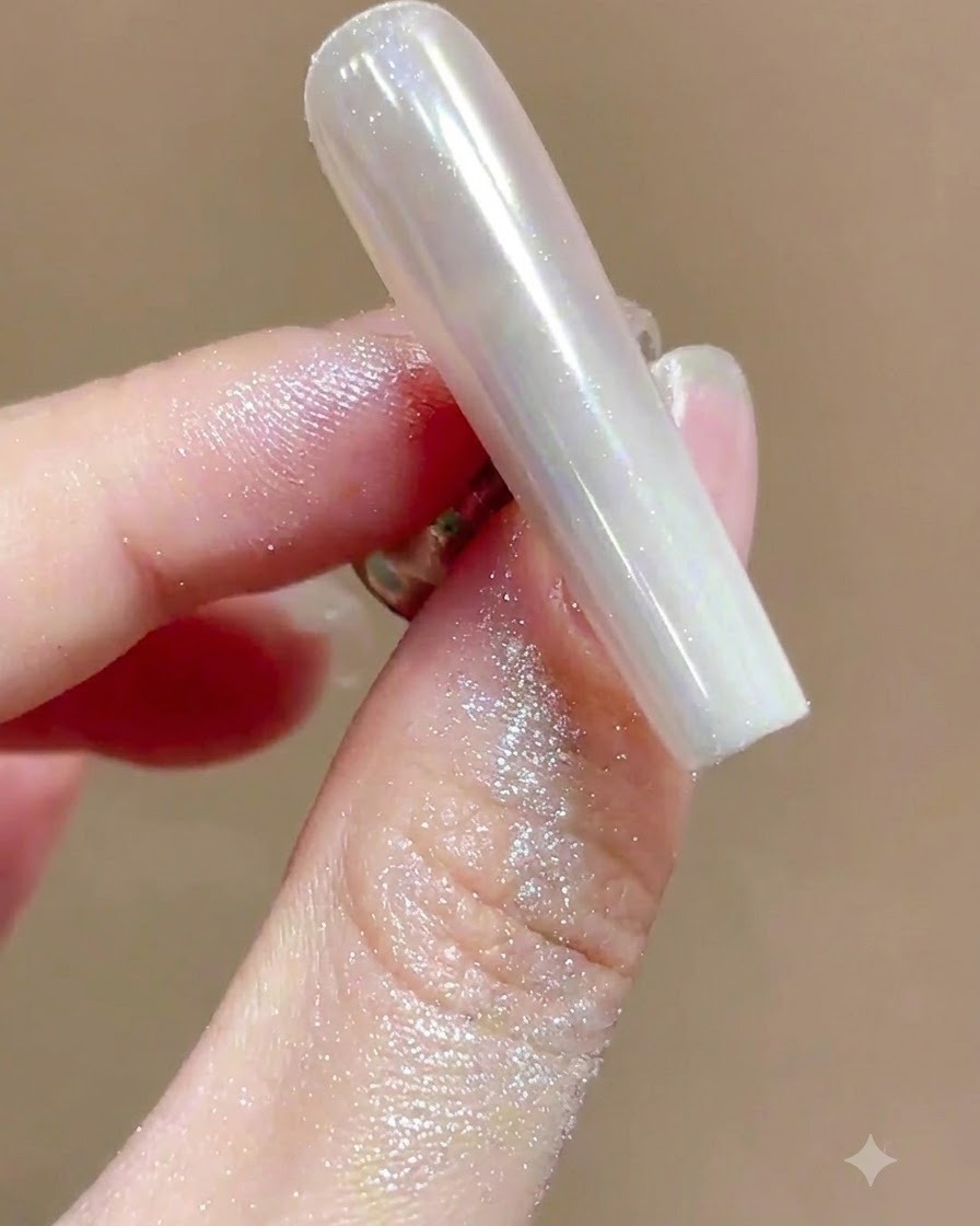 A soft brush sweeping away excess shimmering powder from a high-gloss chrome manicured nail.
