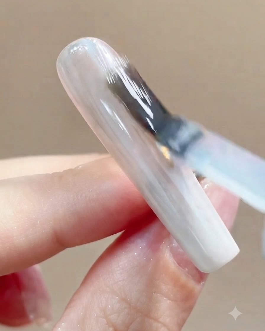 A close-up view of a nail being placed under a UV or LED curing lamp after top coat application.