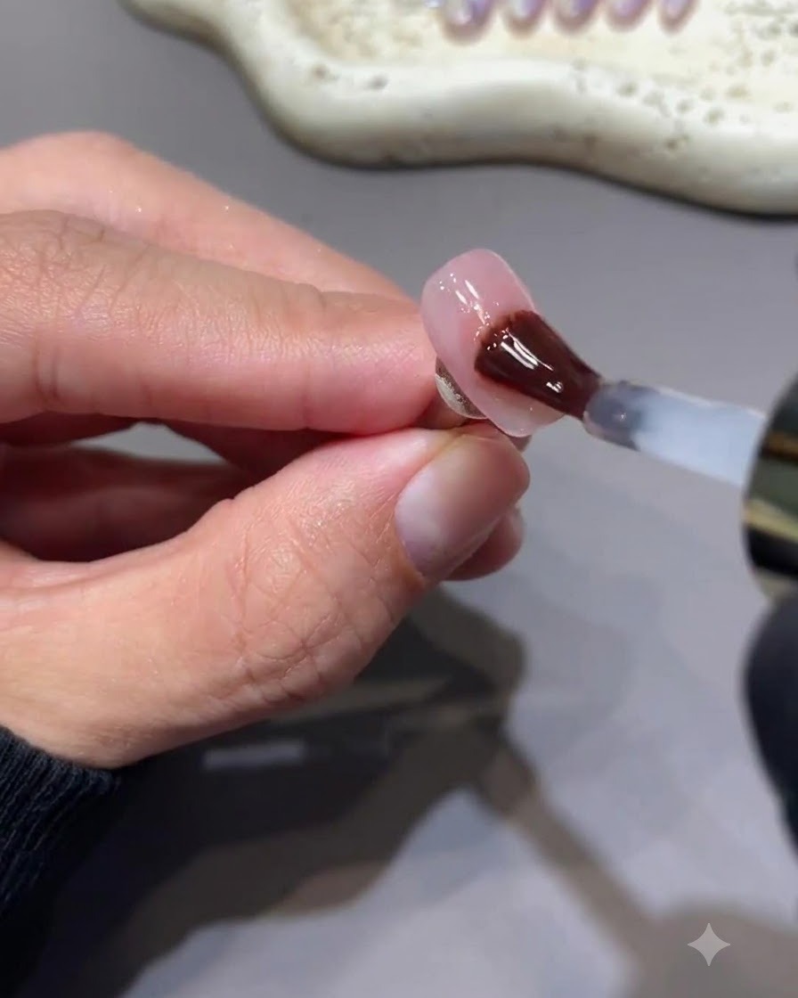 A brush applying a glossy non-sticky gel top coat over a nail with berry pink star art.