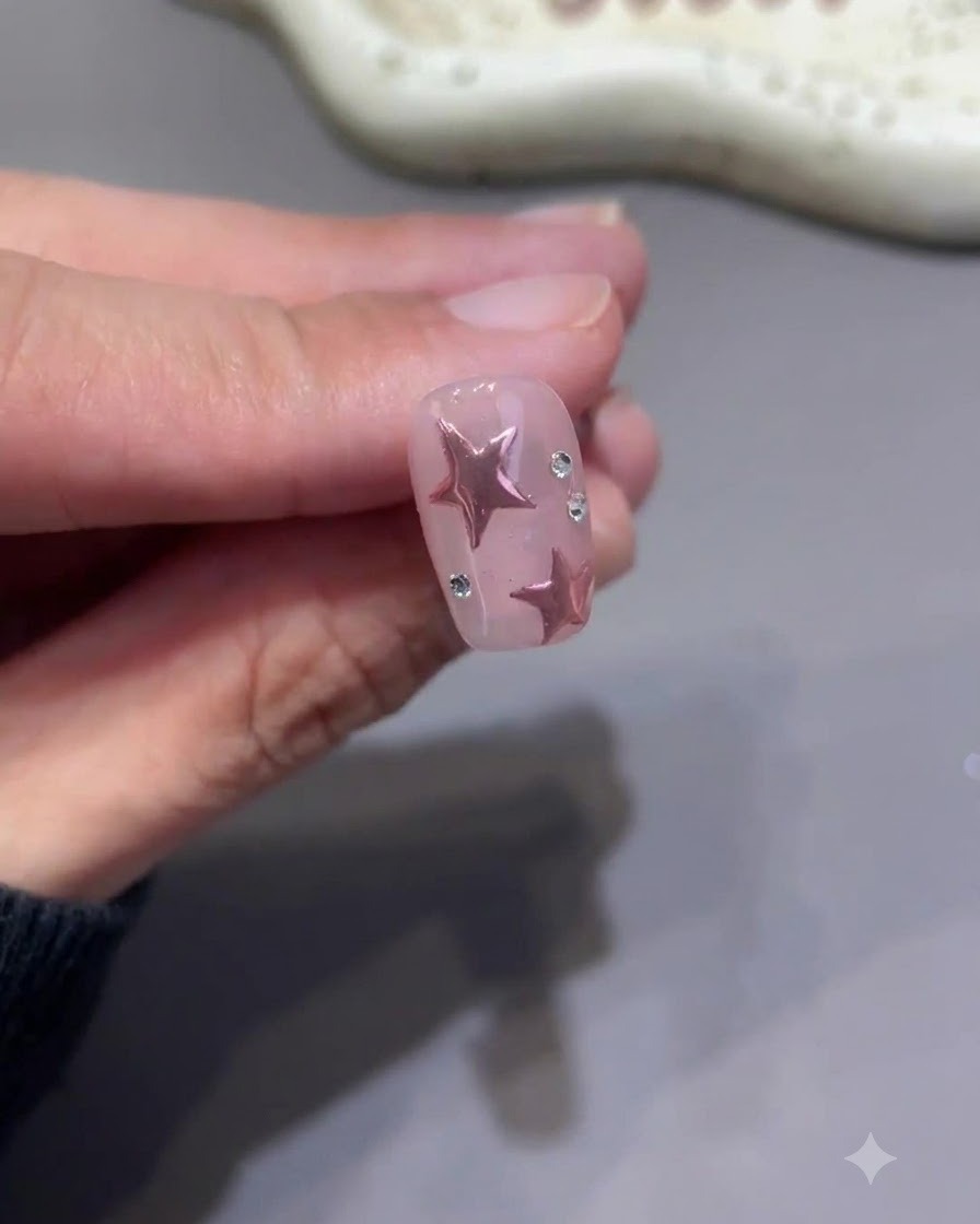 A tiny detail brush meticulously painting top coat around the base of small rhinestones on a finished pink star nail.