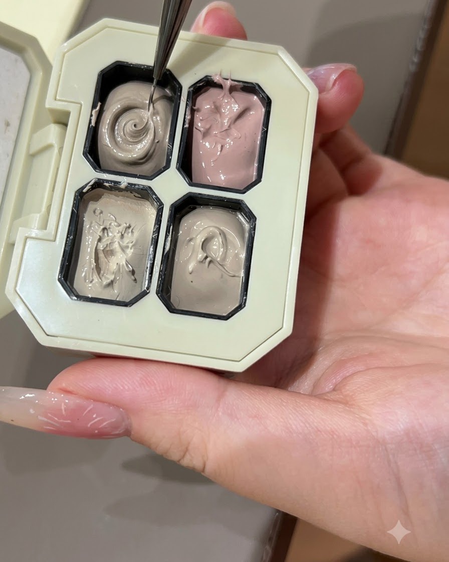 A fine nail art brush picking up grey color gel from a compartment in a palette.