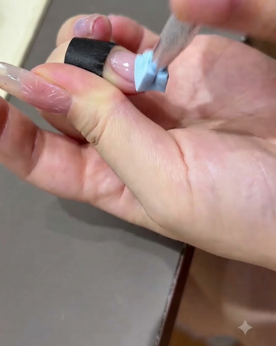 A hand pressing a black practice strip onto the surface of a practice nail plate.