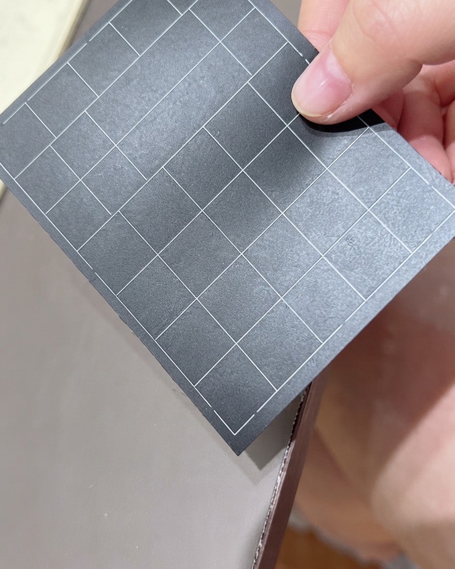 A hand holding a black sheet of grid-lined nail stickers, selecting a sticker.