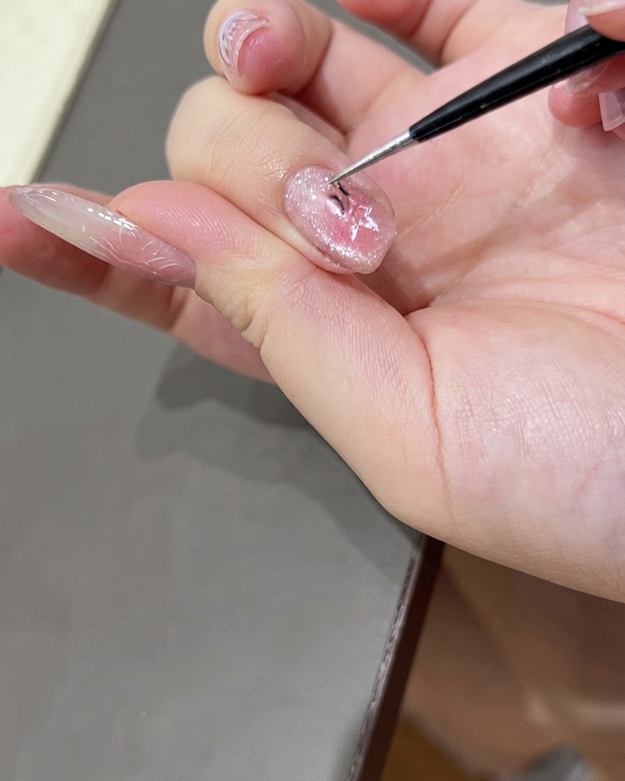A pair of fine tweezers delicately peeling a star-shaped nail sticker off a glossy cat eye gel manicured nail.