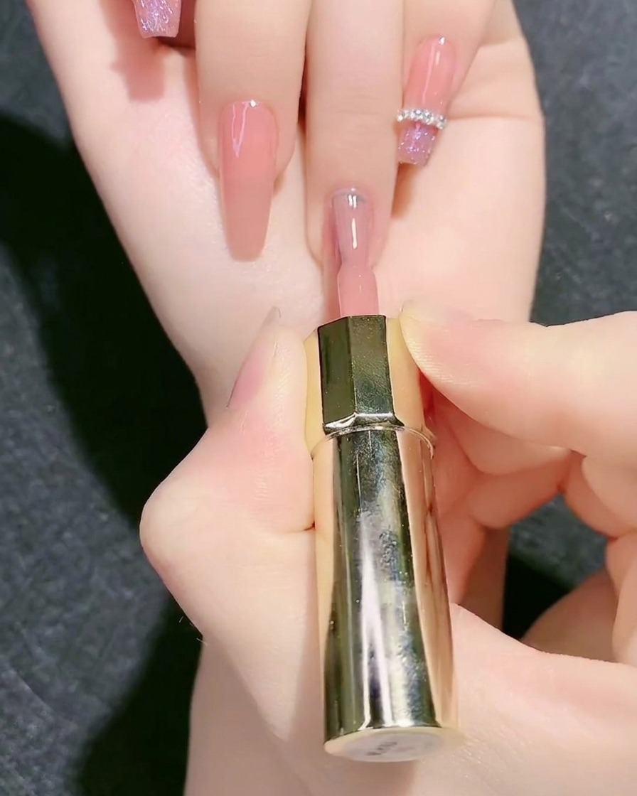 A polish brush applying nude pink gel base color onto a fingernail.