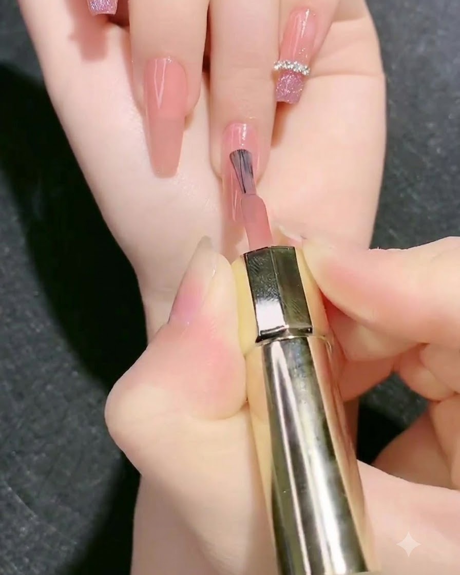 A brush applying a second layer of nude pink base gel onto the fingernail.